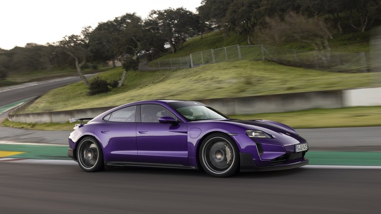 Profile action shot of a purple Porsche Taycan Turbo GT equipped with a rear wing cornering hard on a racetrack.