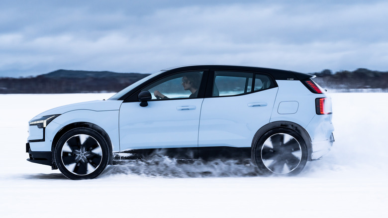 Side profile of a light blue Volvo EX30 electric crossover driving on snow.