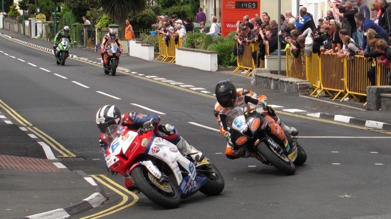 Motorcycle racers lean into a corner at an in-town section of the Isle of Man TT race