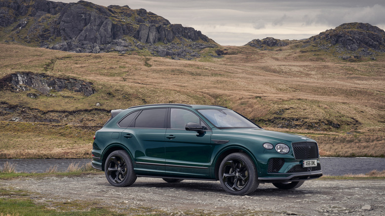 Green Bentley Bentayga S luxury SUV right front three-quarter view parked in front of a sere hillside under gray skies