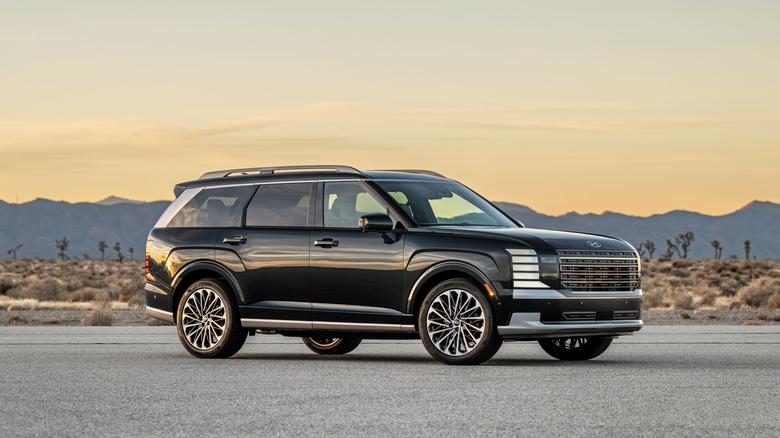 Black 2026 Hyundai Palisade Hybrid Calligraphy model SUV right front three-quarter view parked in a desert at sunset