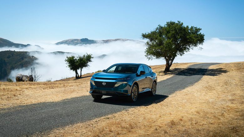 Blue 2026 Nissan Murano SUV left front three-quarter view driving on a high moutain road with clouds in the valley below