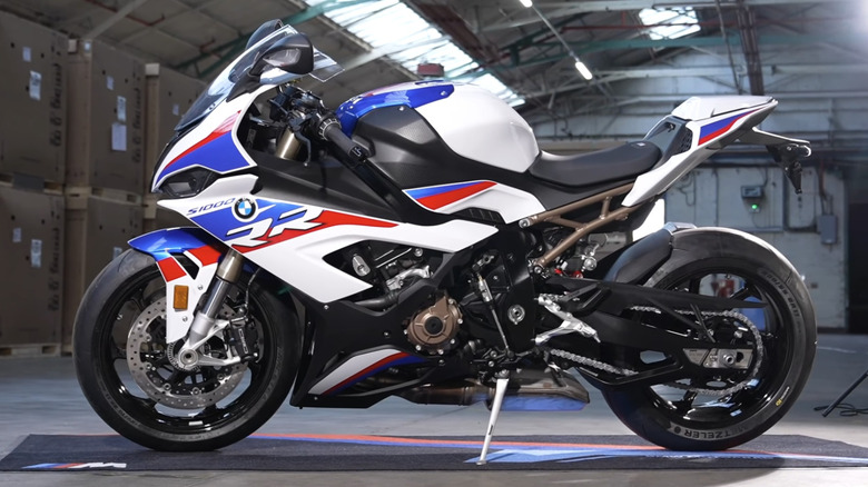 A colorful BMW M 1000 RR stis on a mat in a warehouse.