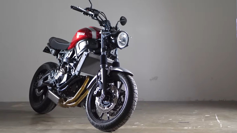 A Yamaha XSR700 sits in an empty room indoors, with light shining off the fuel tank.
