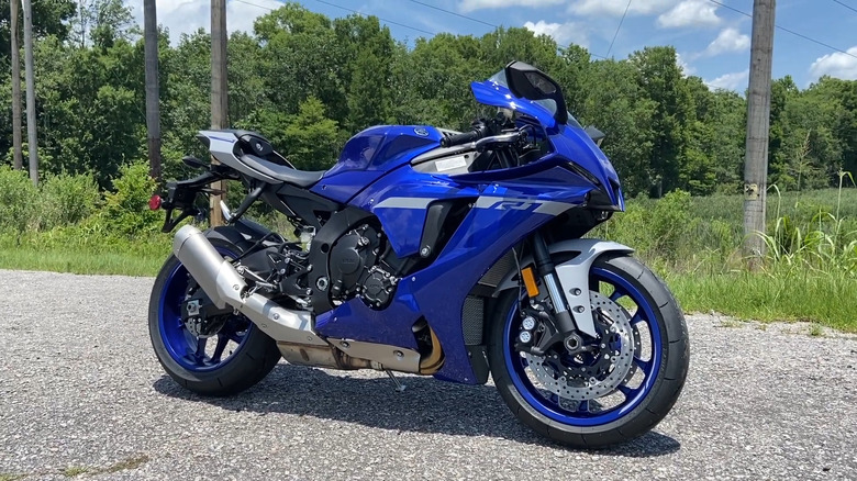 A blue Yamaha YZF-R1 sits parked near trees on pavement.