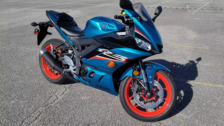 A Yamaha YZF-R3 with a blue and orange color scheme sits in a parking lot with no rider.