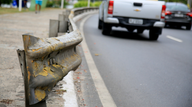 A battered guardrail is in sharp focus while the road ahead blurs away.