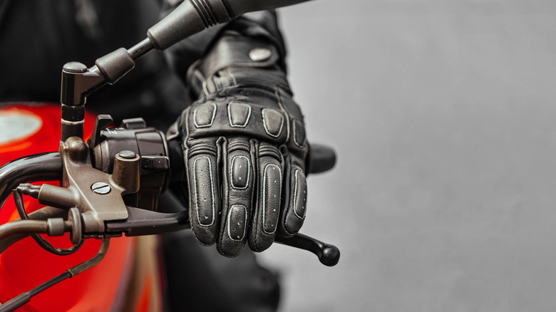 A gloved hand rests over a motorcycle's hand brake, ready to squeeze.