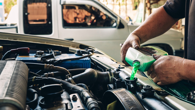 A mechanic pours coolant into a vehicle.