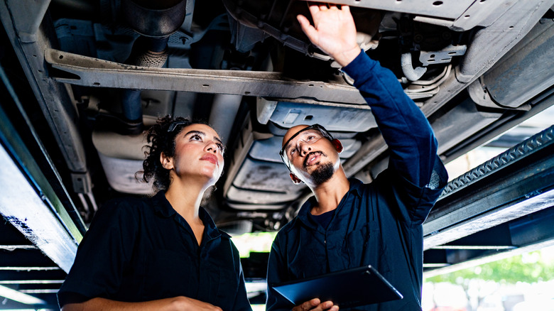 A pair of mechanics inspect a car from below.