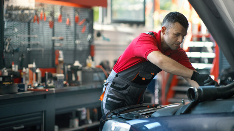 A mechanic works under the hood of a vehicle.