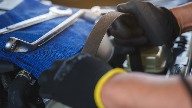 A mechanic wearing gloves removes a serpentine belt.