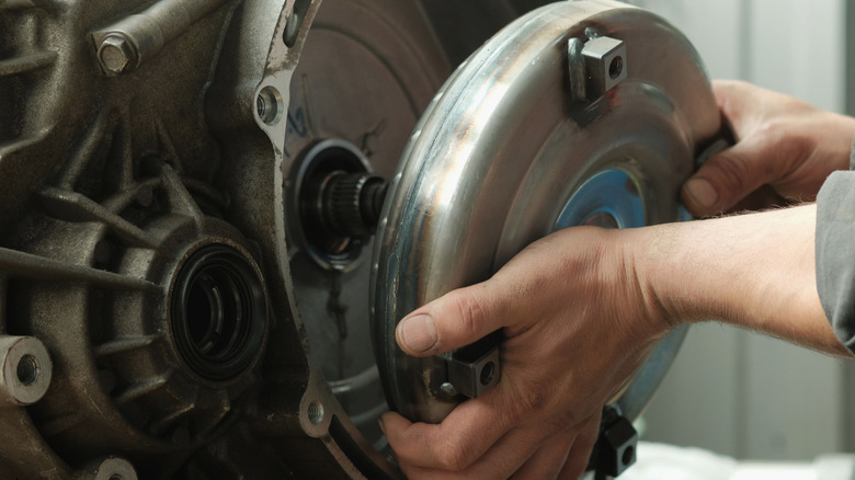 A mechanic removes the torque converter from the transmission.