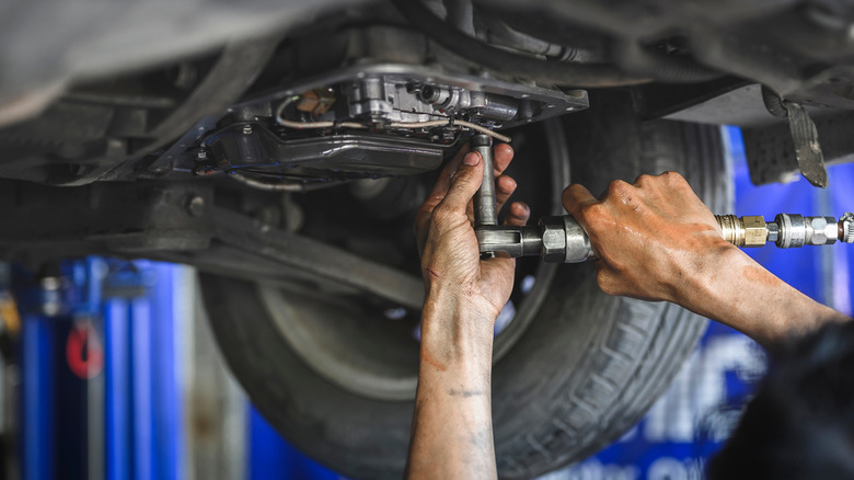 A mechanic works beneath a car for a transmission service.