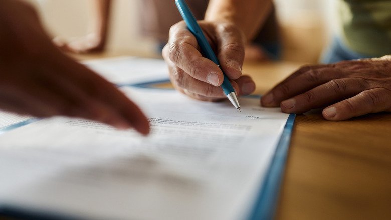 A person signs paperwork with a blue pen.