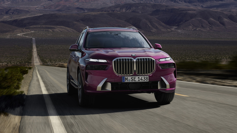 A purple BMW X7 SUV seen in a front view driving on a highway with mountains in the background