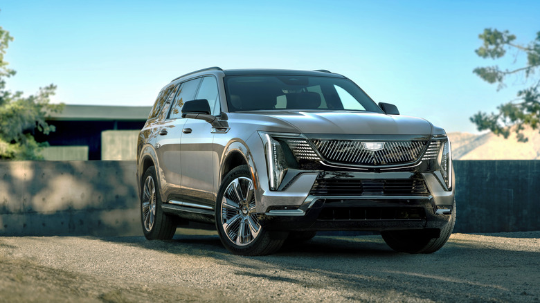 A gray 2026 Cadillac Escalade IQL electric SUV in a right front three-quarter view parked by a concrete wall