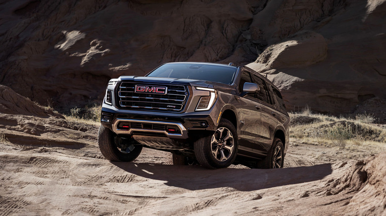 A gray 2025 GMC Yukon AT4 Ultimate in a left front three-quarter view driving off-road