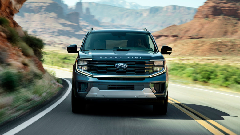 A blue 2025 Ford Expedition SUV in a front view driving on a desert road