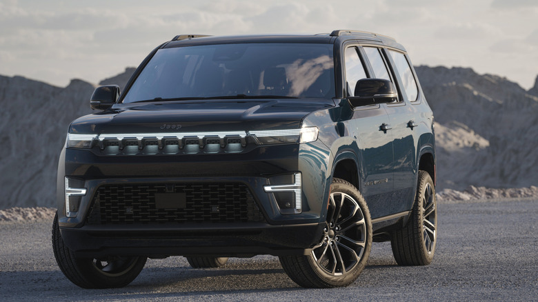 A dark 2026 Jeep Grand Wagoneer SUV in a front left view parked in front of desert mountains