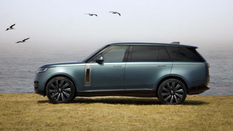 A blue-gray Land Rover Range Rover SV Carmel Edition SUV in a left side view overlooking the ocean with pelicans flying in the background