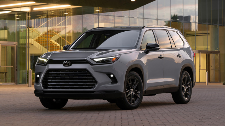 A gray 2026 Toyota Grand Highlander SUV in a left front three-quarter view parked in front of a modern building
