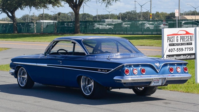 A modified 1961 Chevrolet Impala Bubbletop shows off its rear styling next to a sign