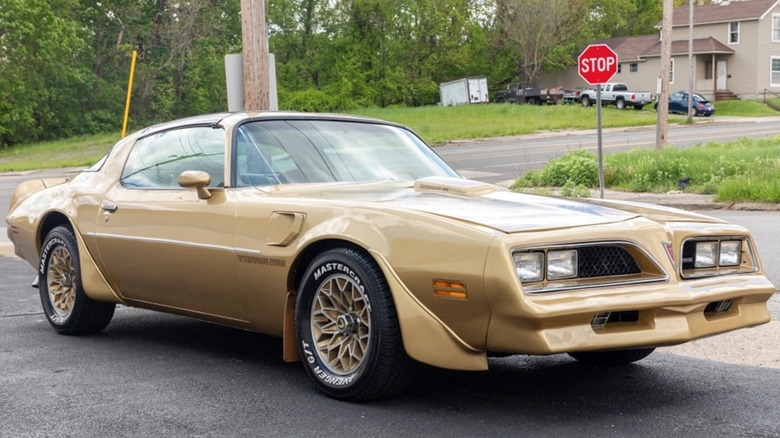 A front 3/4 view of a 1978 Pontiac Trans Am in gold ahead of a stop sign.
