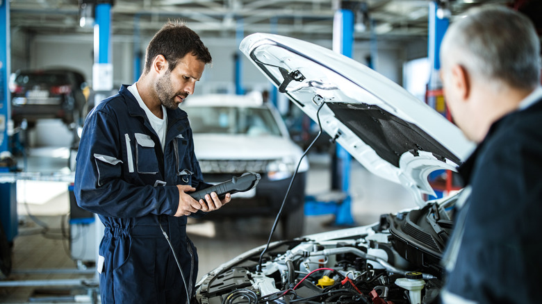 A mechanic works on a car with its hood open.