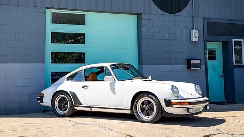 Front 3/4 view of a white 1982 Porsche 911 SC parked in front of a garage door