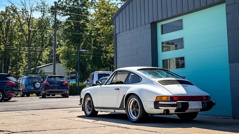 Rear 3/4 view of a white 1982 Porsche 911 SC parked in front of a garage door