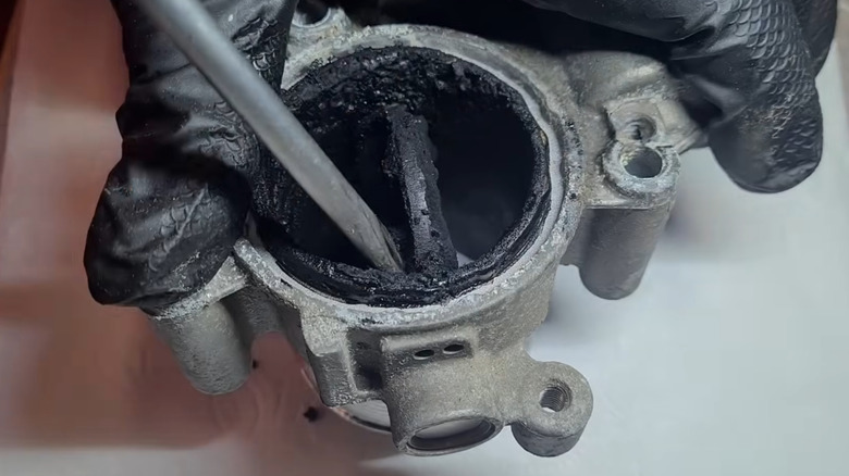 A clogged diesel intake manifold being held by a gloved hand