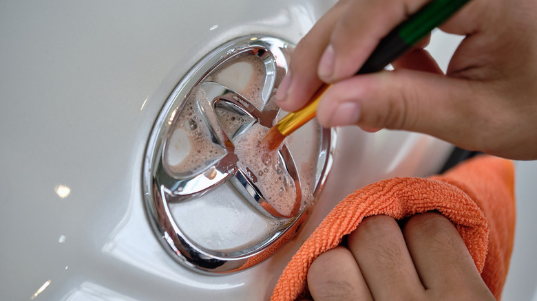 A detailer using a small brush to clean a Toyota badge