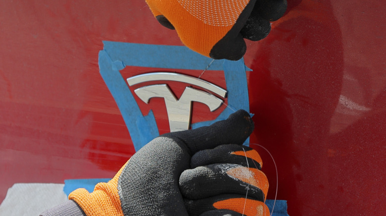 A technician removing the emblem from a Tesla EV using tape and some string
