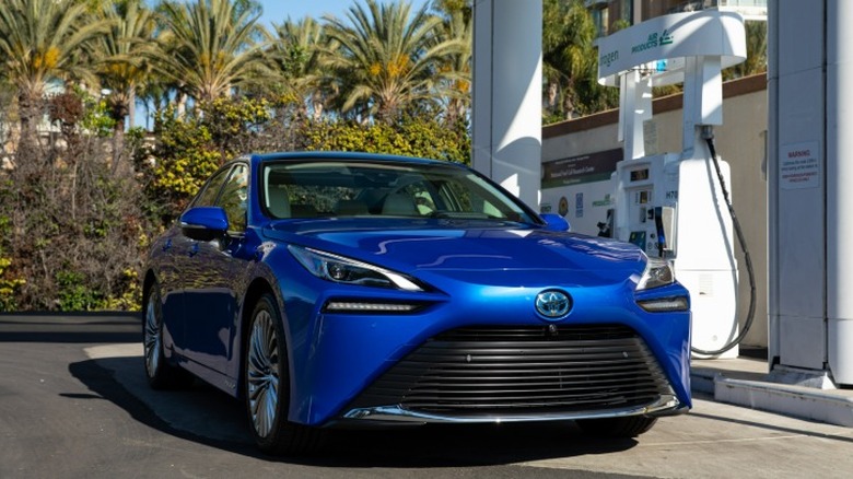 A blue 2021 Toyota Mirai at a gas station with palm trees in the background