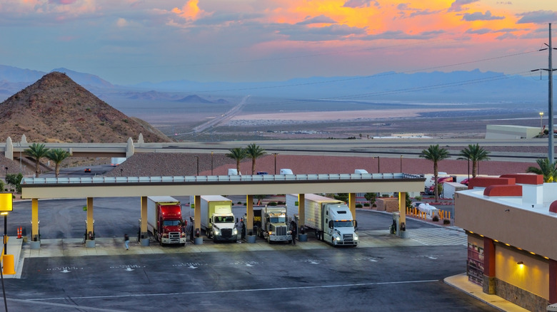 Semi trucks fueling against dramatic evening sky on desert landscape