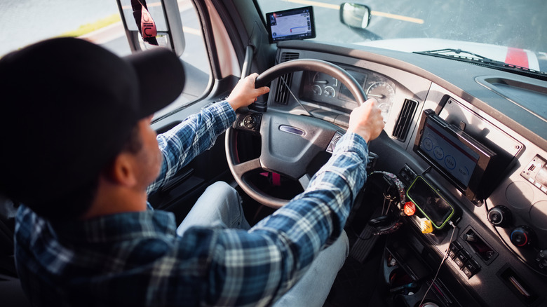 A professional male truck driver wearing casual attire actively driving a modern semi truck