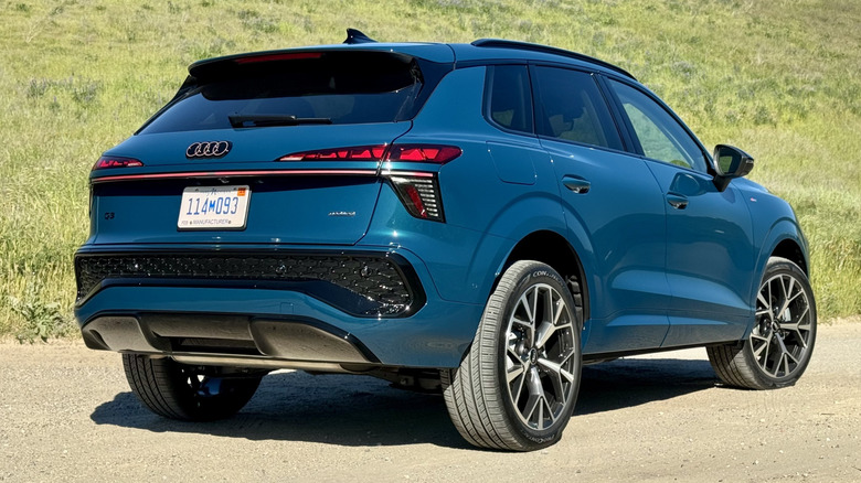 A rear three-quarters shot of the blue Q3 parked on dirt in front of a grassy hill