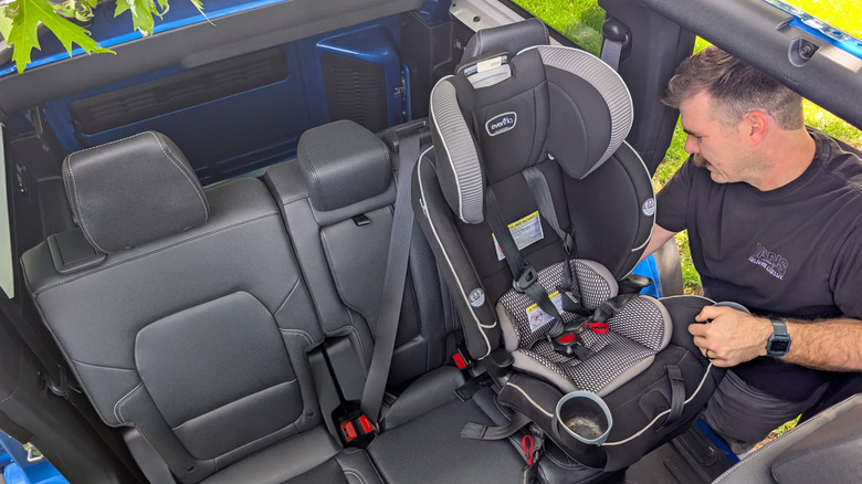 A man in a black t-shirt puts a toddler seat in the back of a Ford Bronco