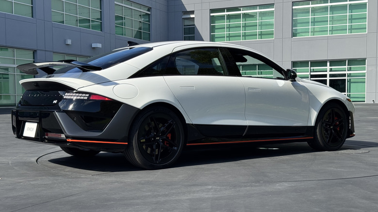 rear three-quarters shot of the white Ioniq 6 N parked on asphalt in front of a gray building