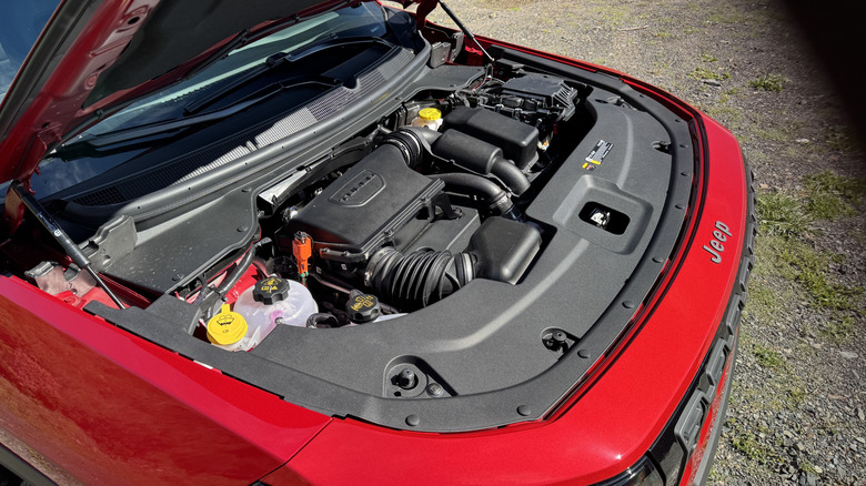 An underhood shot showing the red Cherokee's turbocharged hybrid engine with gravel in the background