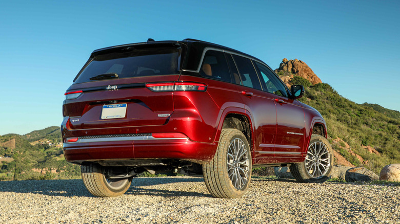 rear three quarters shot of a red Jeep Grand Cherokee parked on gravel in front of a shrub-covered mountain