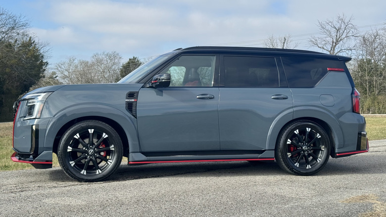 A side view of the gray Armada Nismo parked on asphalt in front of grass and trees