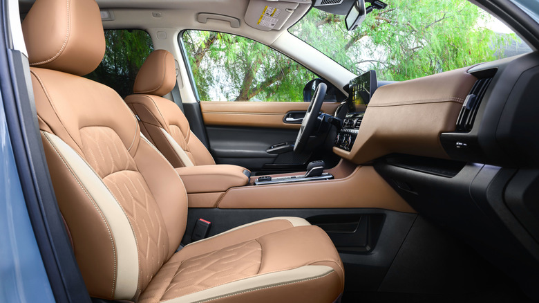 A look in the passenger door showing the quilted brown leather on a Pathfinder Platinum with green trees out the windows