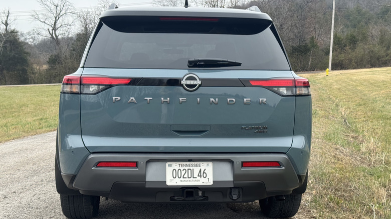 A rear shot of the teal Pathfinder Platinum parked on asphalt next to grass in front of trees