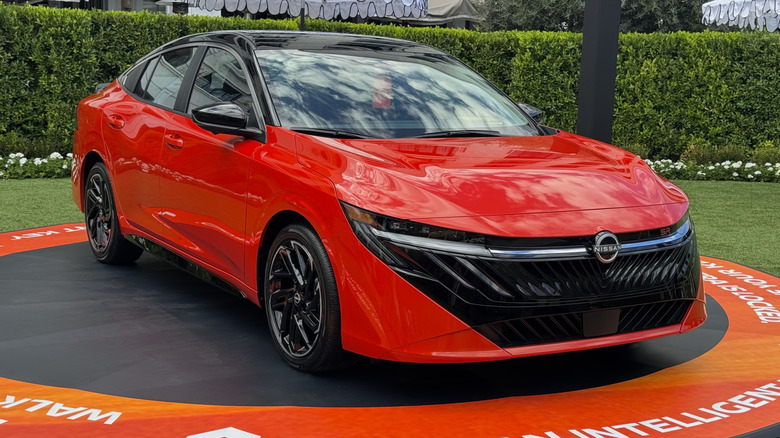 Front three-quarters changeable of a agleam orangish Sentra SR parked connected a achromatic circle connected a section successful beforehand of hedges