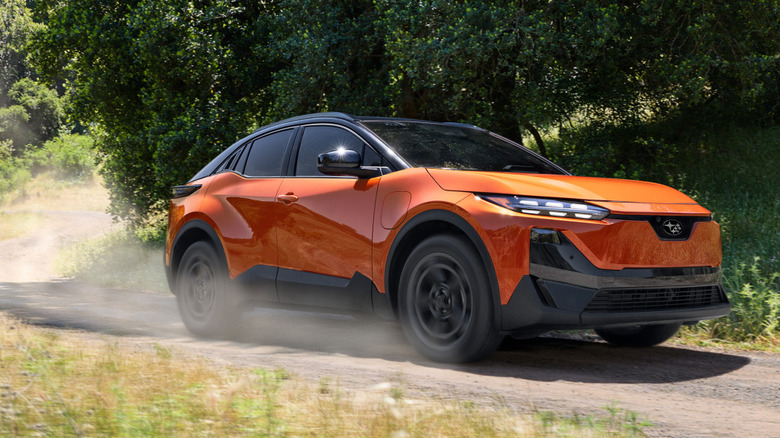 A front three-quarters shot of an orange Uncharted driving on a dirt road in front of trees