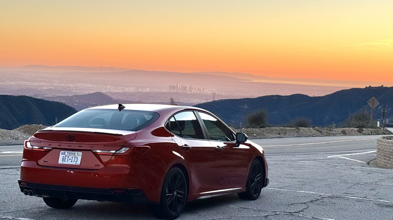 A rear three quarters shot of the red Camry parked on asphalt in front of a gorgeous view of the LA basin at sunset