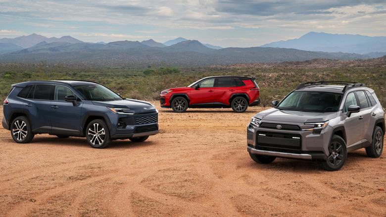 The family of 2026 RAV4 PHEV trims, with a gray Woodland in front, a blue XLE next to it, and a red GR Sport in the background parked on dirt in front of a desert scape