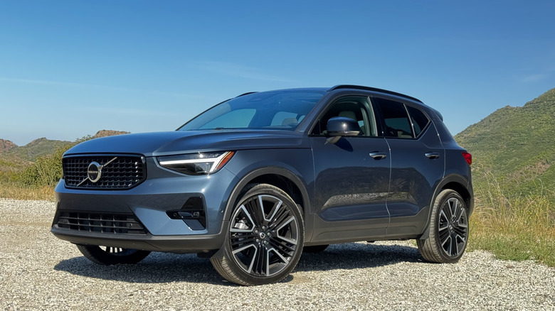 Front three-quarters shot of the dark blue Volvo XC40 parked on gravel in front of a blue sky and a skyline of green mountains